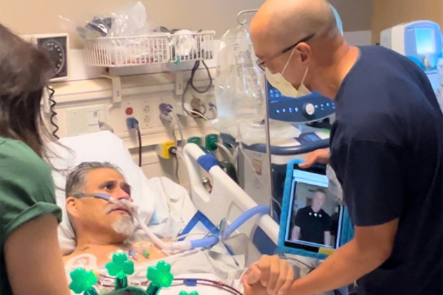 保罗·阿吉拉尔躺在病床上，护士大卫·山田站在他身边，握着他的手. 山田还拿着一个写着史泰龙留言的平板电脑.